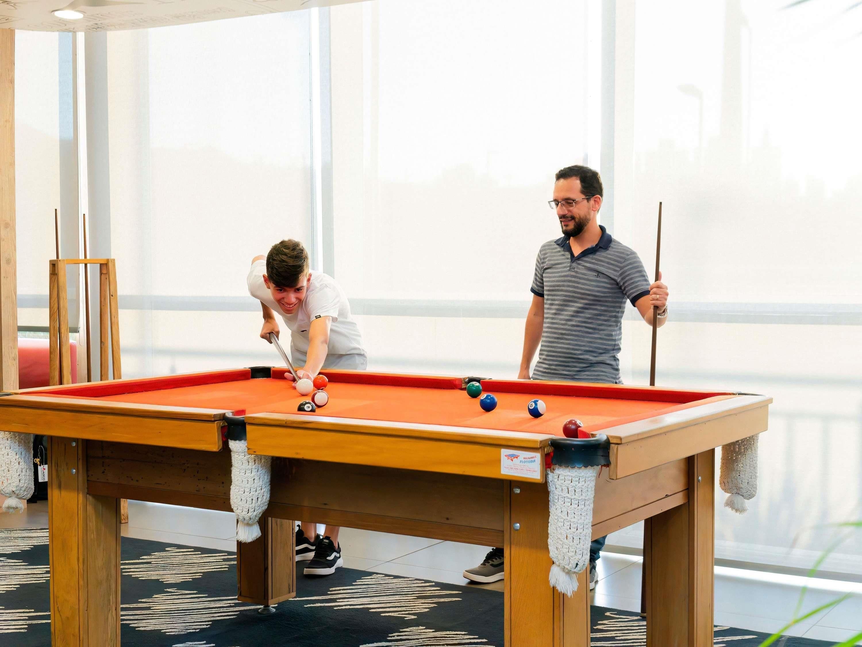 Une table de billard avec des billes et des queues, un socle en bois et un chemin de table tissé.