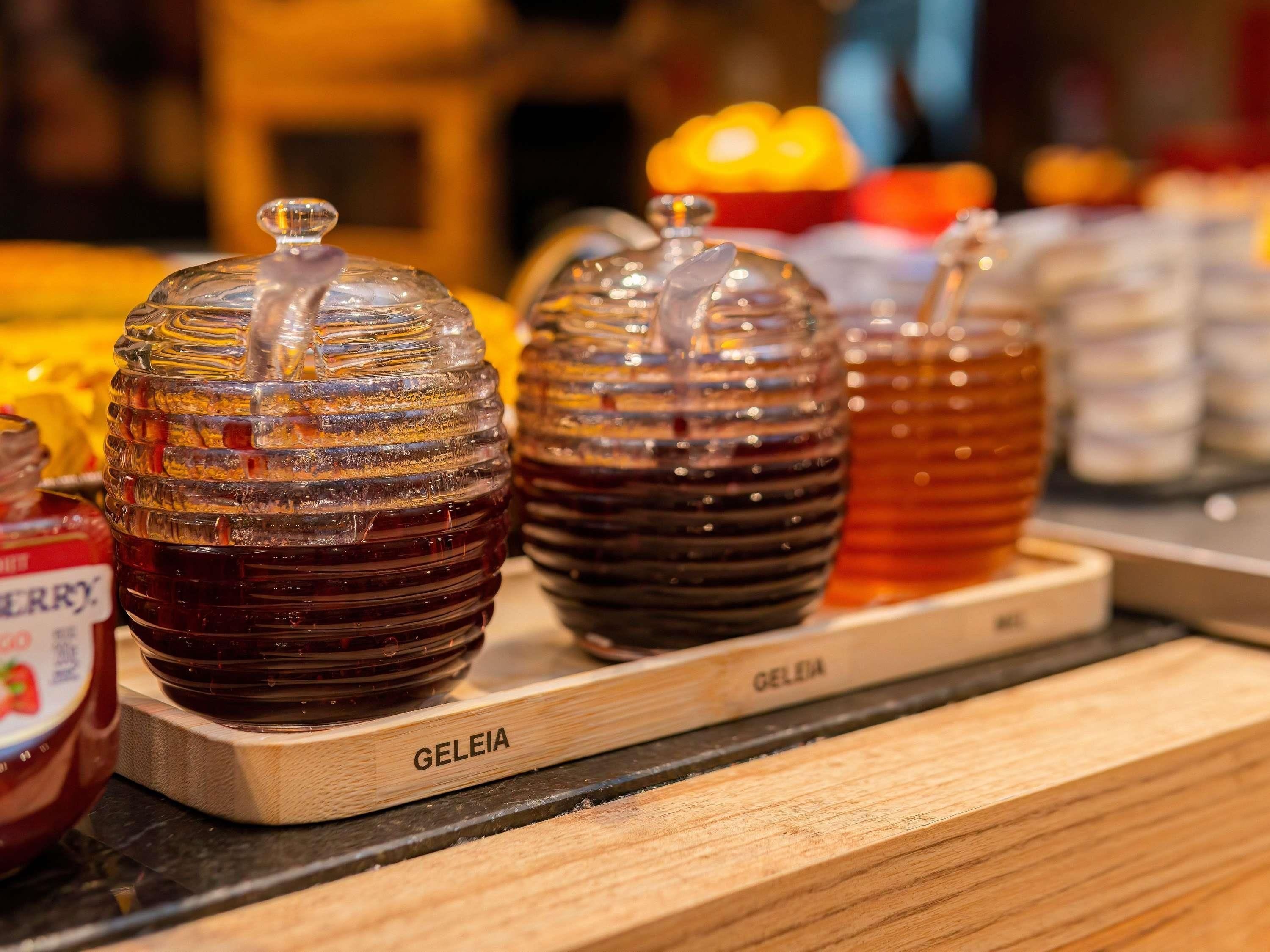 A display of honey jars on a wooden board with the label 'GELEIA'.