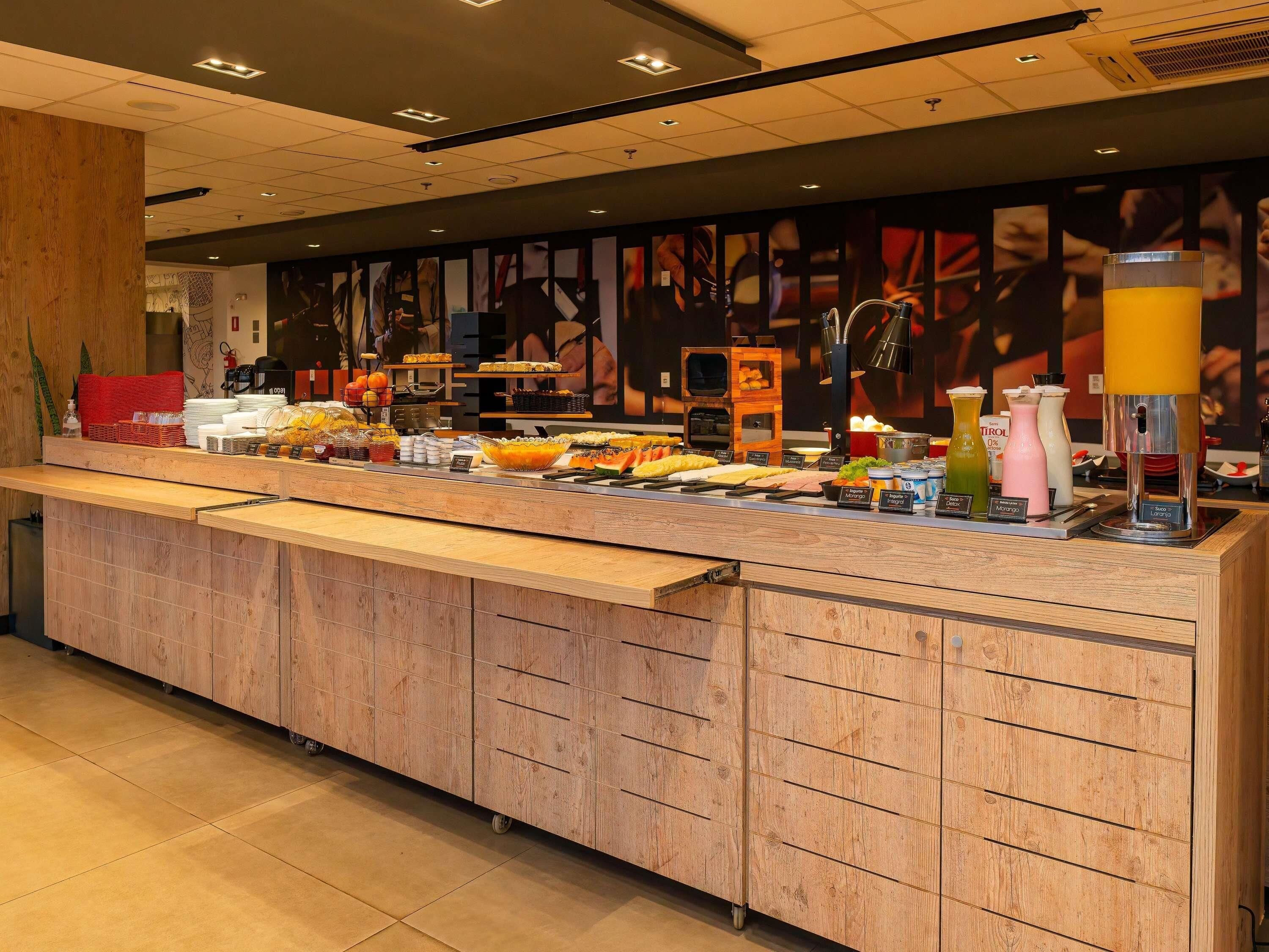 Uma área de buffet com diversas opções de comida e bebida, incluindo uma máquina de café e um dispensador de suco.