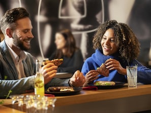Deux personnes sont attablées dans un restaurant, devant une table où se trouvent une boisson et une assiette de nourriture.
