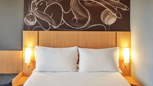 A hotel room with a large bed, two bedside tables with lamps, and a wall art piece above the bed. - ibis Londrina Shopping (Londrina)