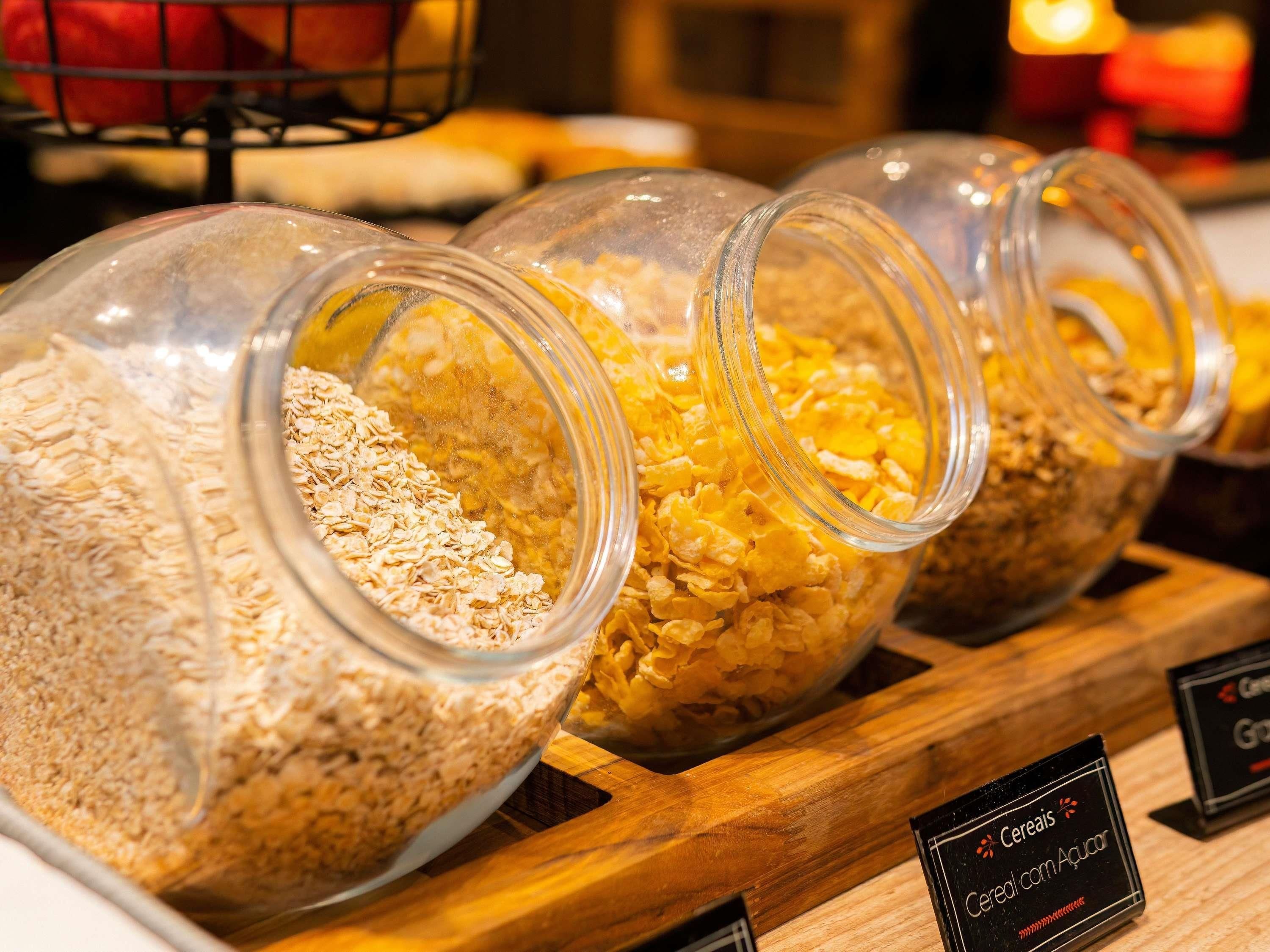 A display of cereal varieties in glass jars on a wooden board with labels.