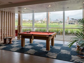 A pool table in a room with large windows, a wooden partition, and a view of a cityscape. - ibis Londrina Shopping (Londrina)