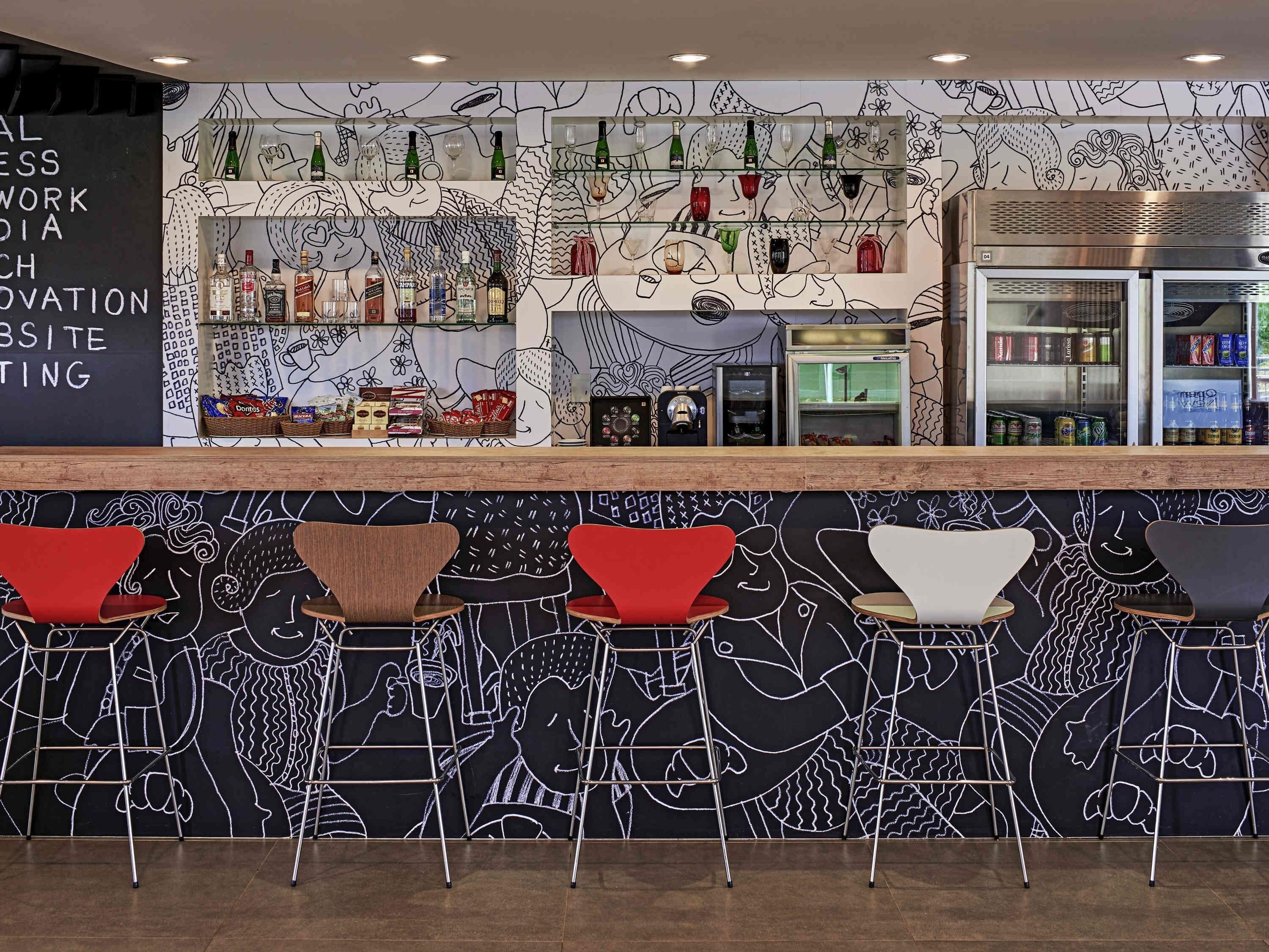 A bar area with a mural, shelves with bottles, and a refrigerator.