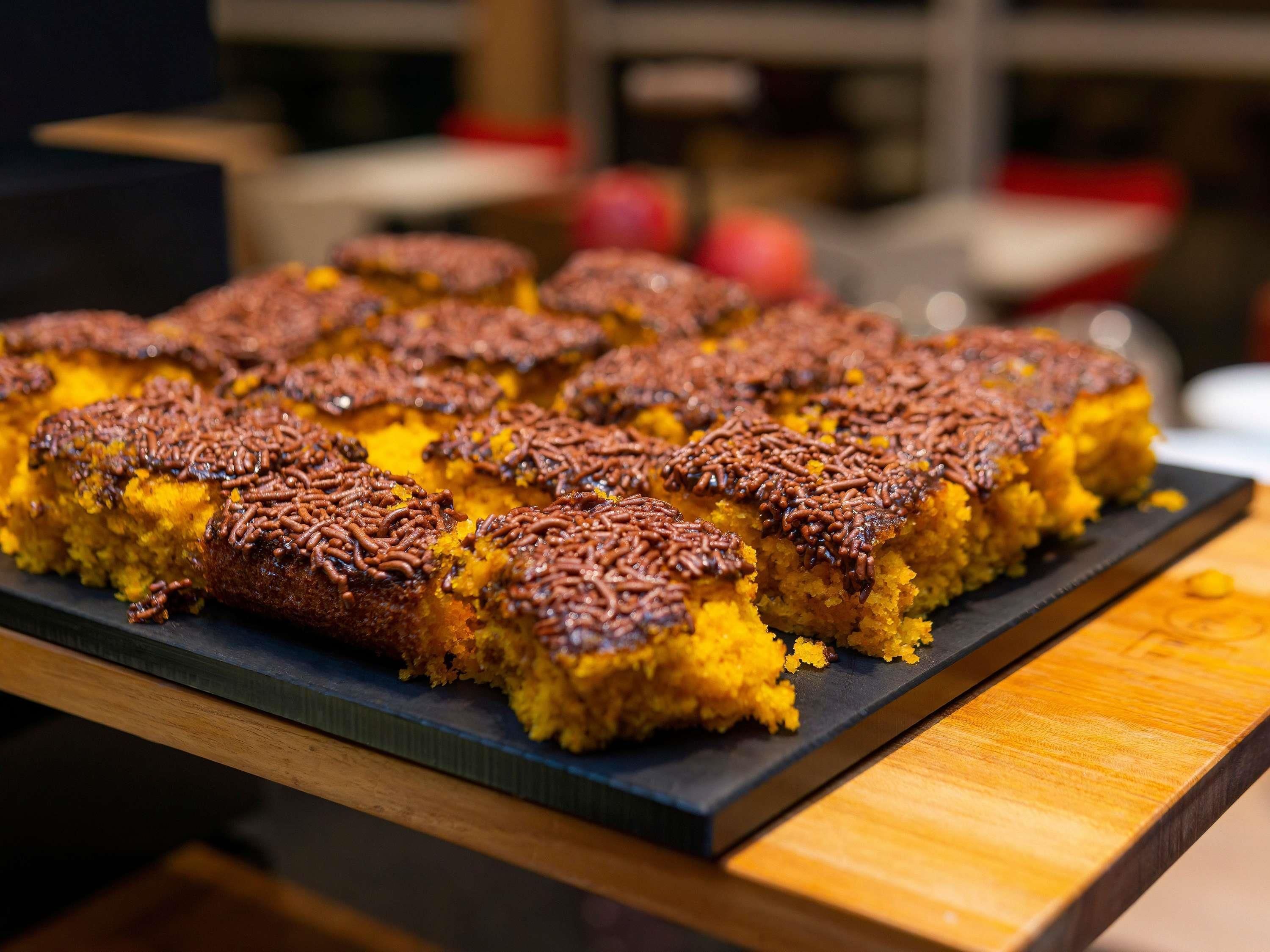 A tray of square-shaped food items with a golden-brown crust, possibly a type of dessert or baked good, on a dark slate serving board.