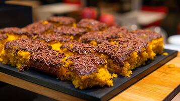 A tray of square-shaped food items with a golden-brown crust, possibly a type of dessert or baked good, on a dark slate serving board.