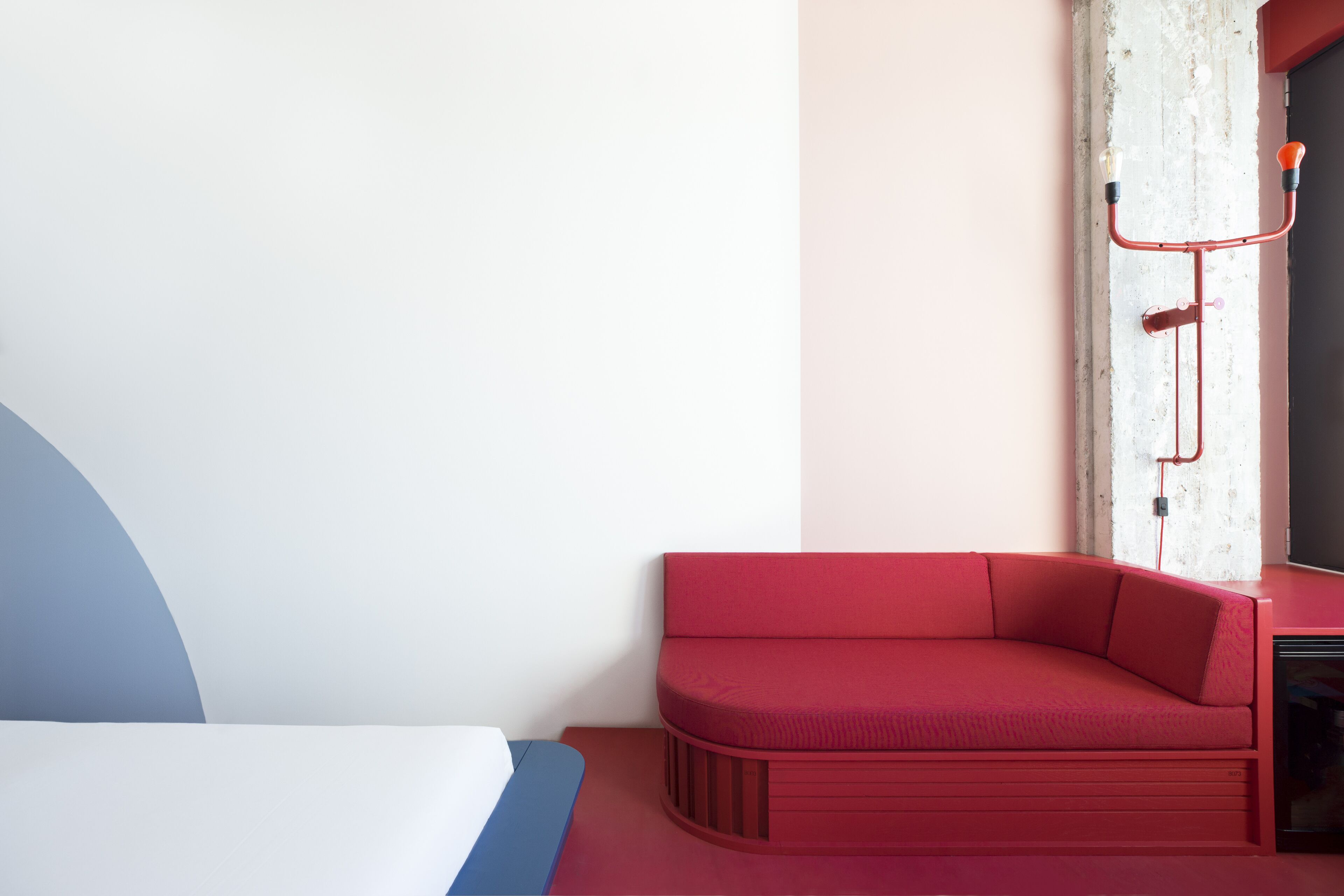 A modern room with a red sofa, a bed with a blue and white headboard, and a white pillar with a red light fixture.