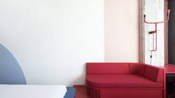 A modern room with a red sofa, a bed with a blue and white headboard, and a white pillar with a red light fixture.
