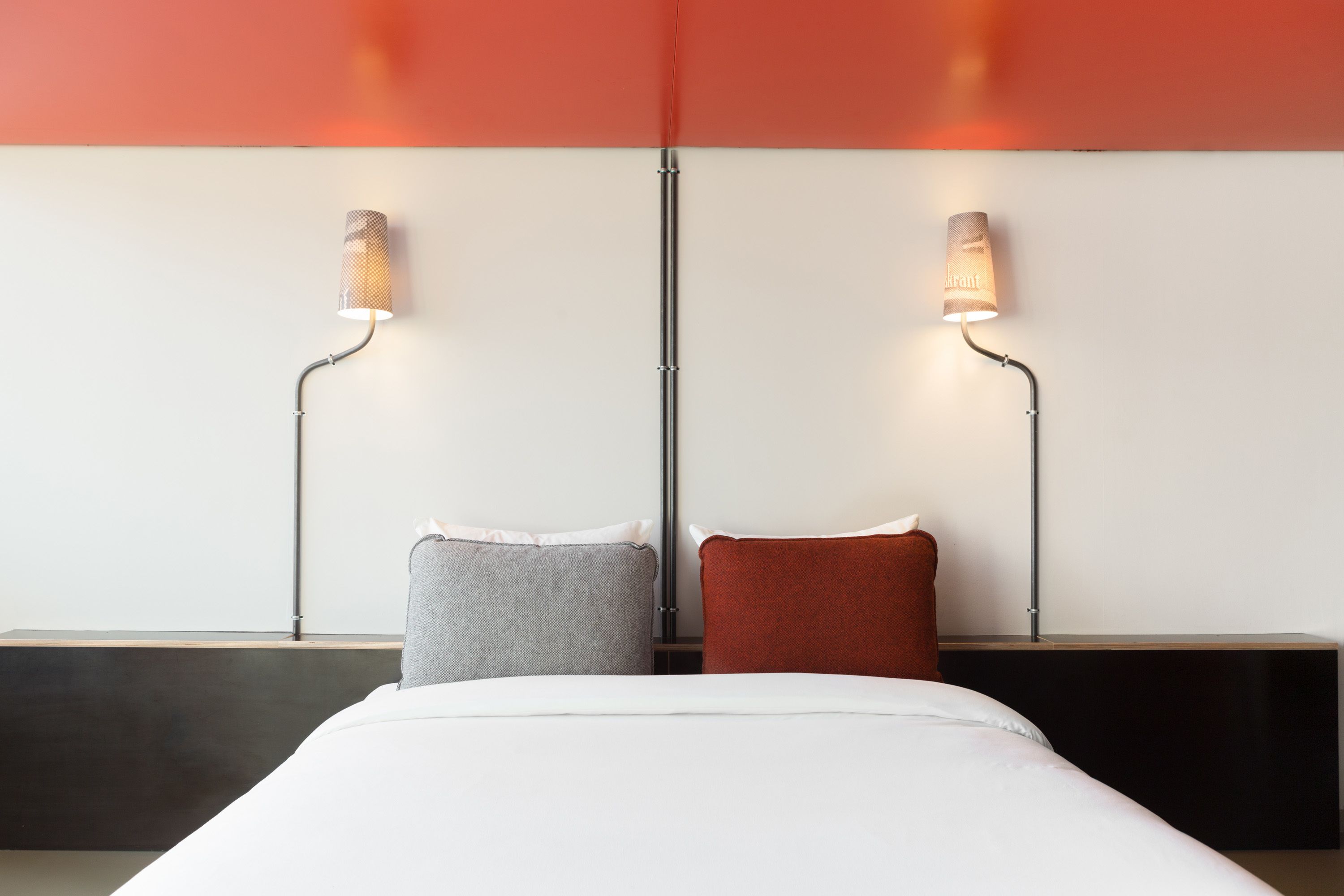 Camera d'albergo moderna con un letto grande, due lampade ai comodini e una parete a contrasto rosso e bianco.