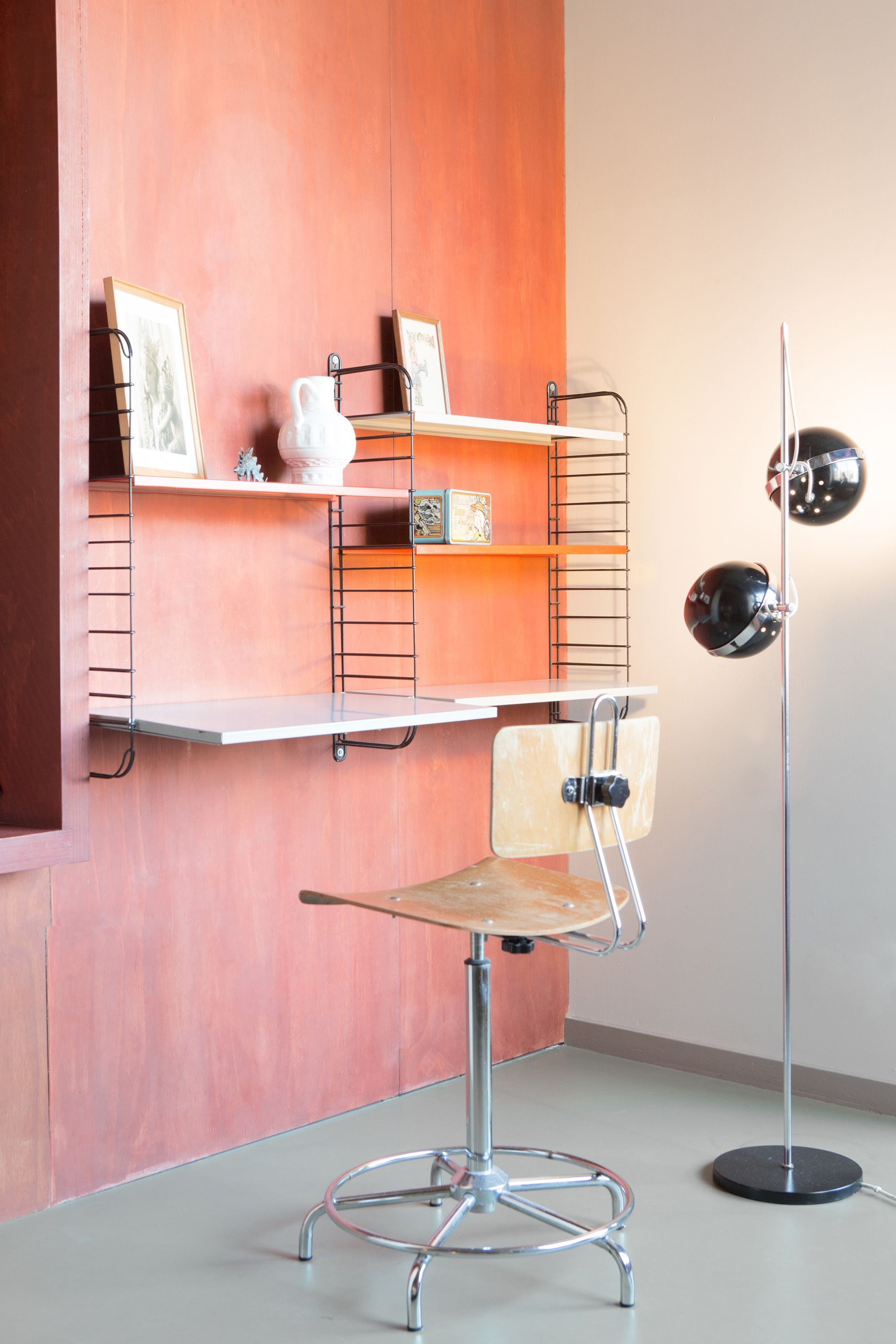 Un espacio de trabajo moderno con escritorio, silla, estanterías y una lámpara de pie.