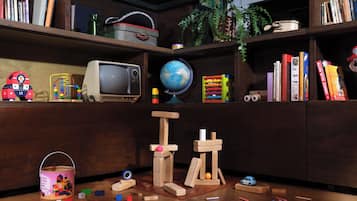Une pièce avec une bibliothèque en bois remplie de livres, un globe terrestre, une voiture jouet et un téléviseur d’époque.