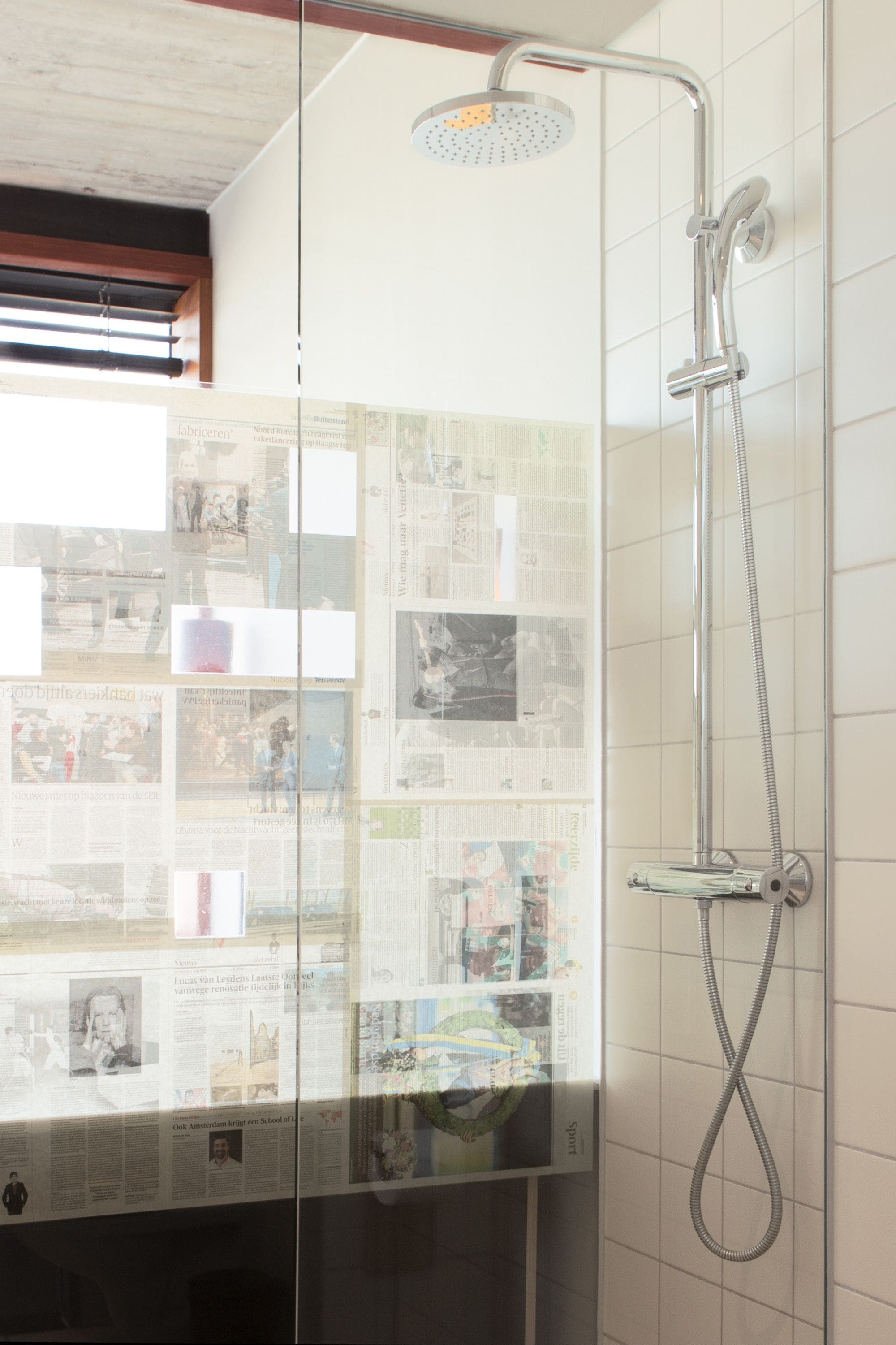 A shower with a glass door and a newspaper collage on the wall.