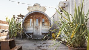 A wooden sauna structure with a sign reading "SAUNA" and a wooden deck in front.