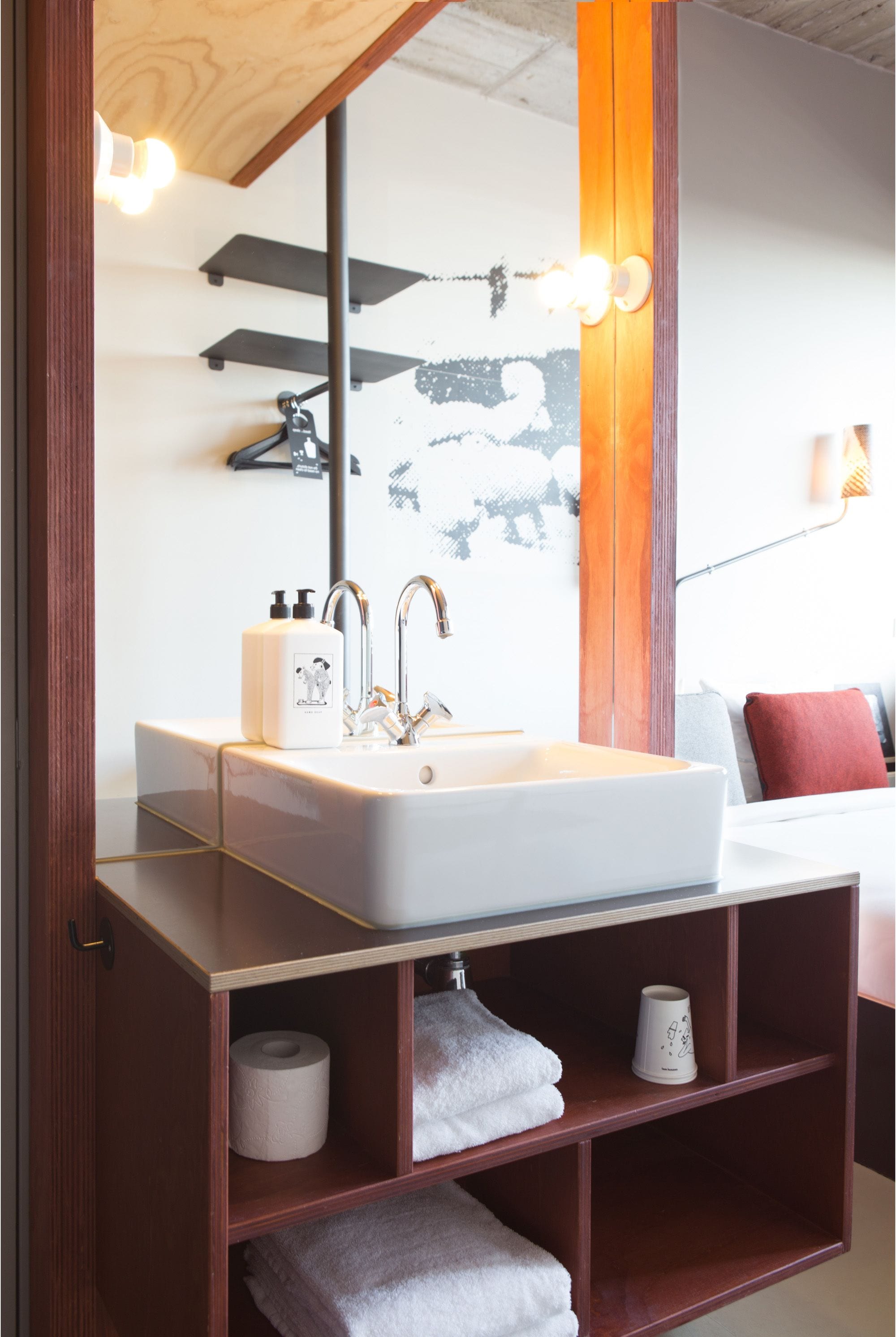 Une salle de bain avec un lavabo blanc, des étagères en bois, un miroir et un porte-serviettes.