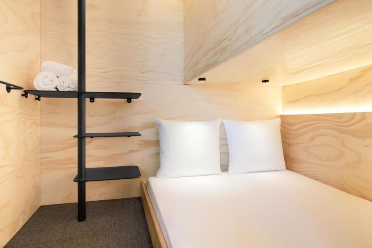 A compact room with a bunk bed, a shelf with towels, and a small bedside table.