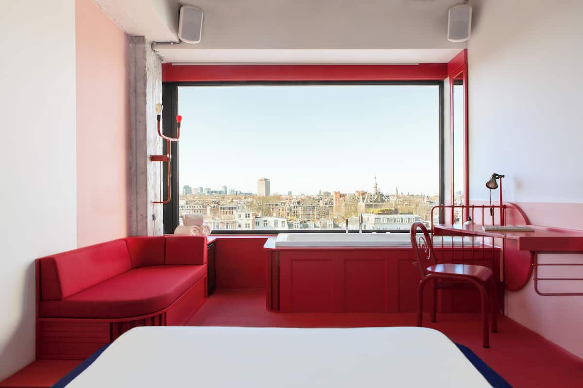 Habitación con decoración roja, vista a la ciudad, cama, escritorio y una silla.