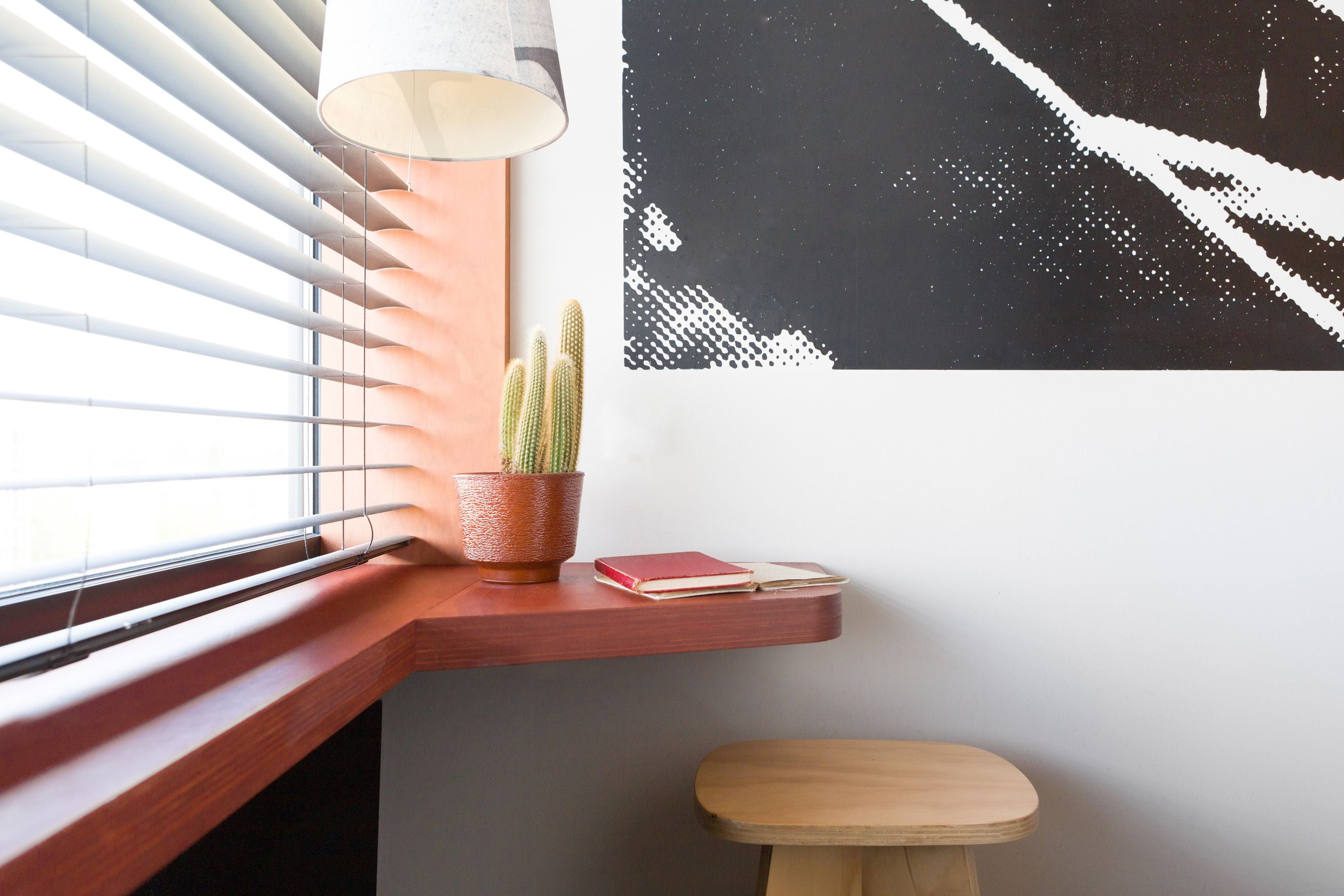 Un coin avec un banc en bois, un cactus dans un pot en terre cuite et une lampe fixée au mur.