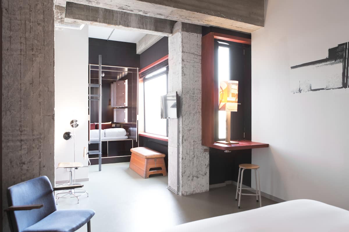 Habitación de hotel moderna con cama, escritorio, silla, taburete y armario.