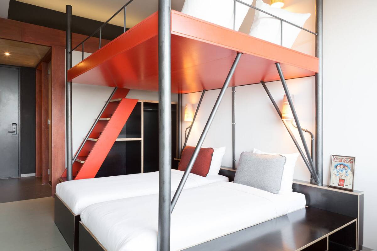 Una habitación de hotel moderna con una litera, una escalera, una mesita de noche y un cuadro enmarcado.