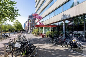 Un hotel moderno con un toldo rojo, bicicletas estacionadas afuera y una vista despejada de la calle.