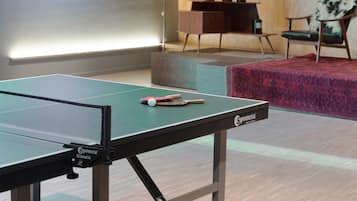 Une table de ping-pong avec une raquette et une balle, un meuble en bois et une chaise agrémentée d’un coussin décoratif.