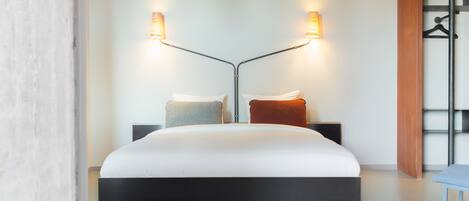 A modern hotel room with a large bed, two bedside tables, and a wall-mounted TV.