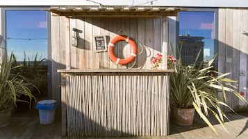 A wooden bar area with a life ring, a chalkboard menu, and potted plants.