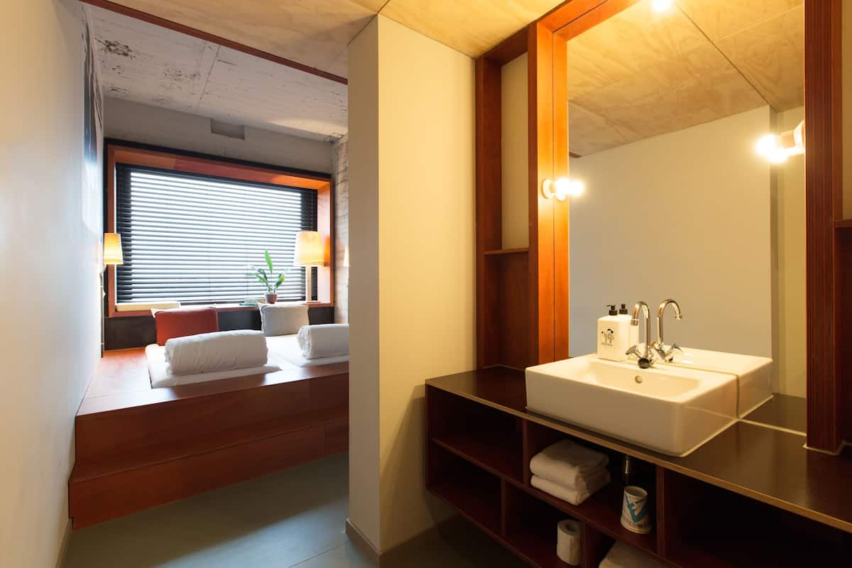 Un baño con tocador de madera, un espejo grande, un lavamanos y una ventana con persianas.