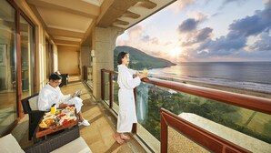A balcony with a dining table set with food and drinks, a person reading, and another person looking out at the ocean. - The Westin Zhujiajian Resort, Zhoushan (Zhoushan)