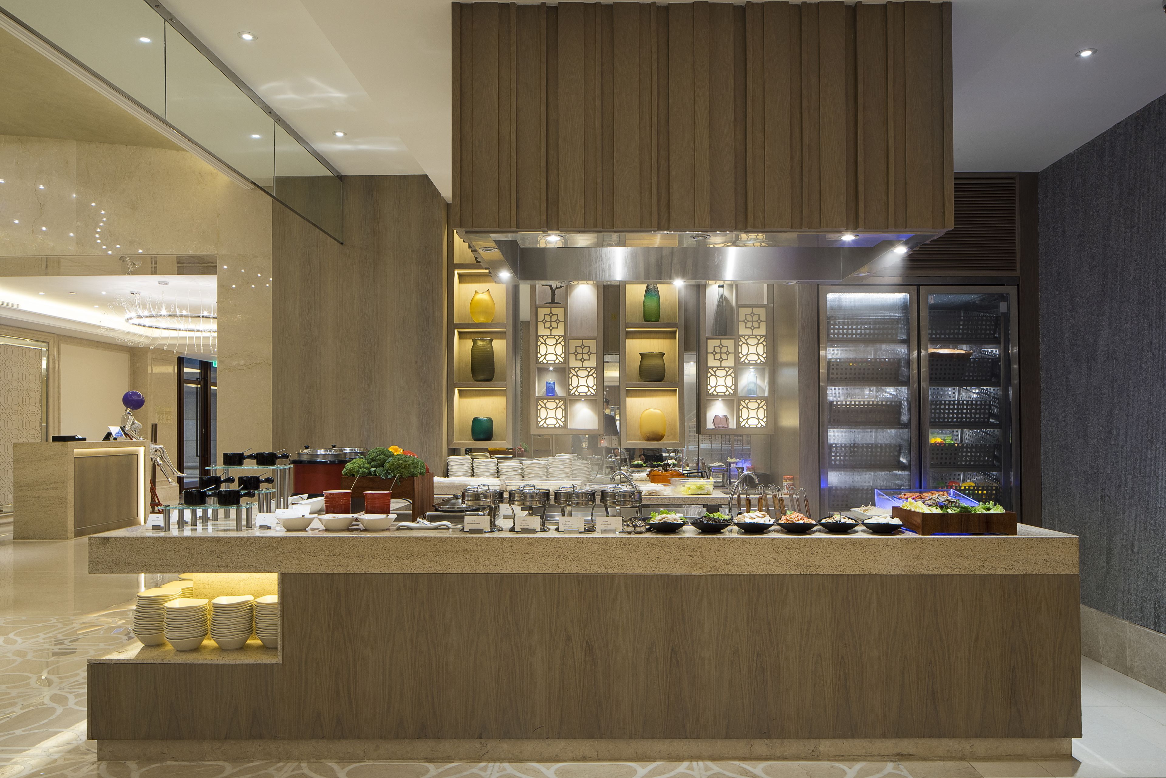 A modern hotel lobby with a central reception desk, a decorative wall with patterned lights, and a glass display case with various items.