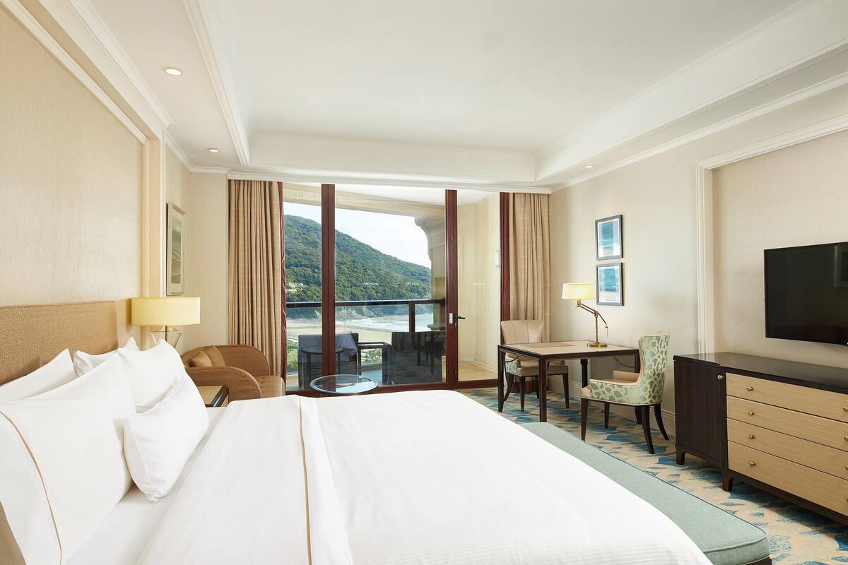 Une chambre d’hôtel avec un grand lit, un bureau, une chaise, une télévision et une vue sur les montagnes.