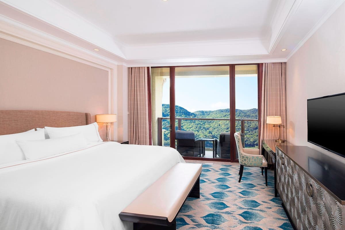 Une chambre d’hôtel avec un grand lit, une télévision, un bureau avec une chaise et un balcon offrant une vue sur les montagnes.