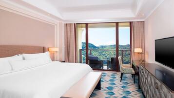 Ein Hotelzimmer mit einem großen Bett, einem Fernseher, einem Schreibtisch mit Stuhl und einem Balkon mit Bergblick.