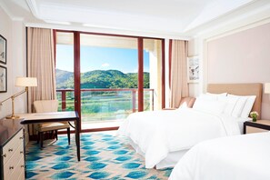 A hotel room with a large window offering a view of green hills, a bed with white linens, a desk with a lamp, and a chair. - The Westin Zhujiajian Resort, Zhoushan (Zhoushan)