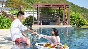 Relax by the pool surrounded by lush greenery and a traditional structure.
