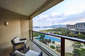 Ein Balkon mit Korbmöbeln, der auf einen Swimmingpool und die Umgebung eines Resorts mit Gebäuden und Bergen blickt.