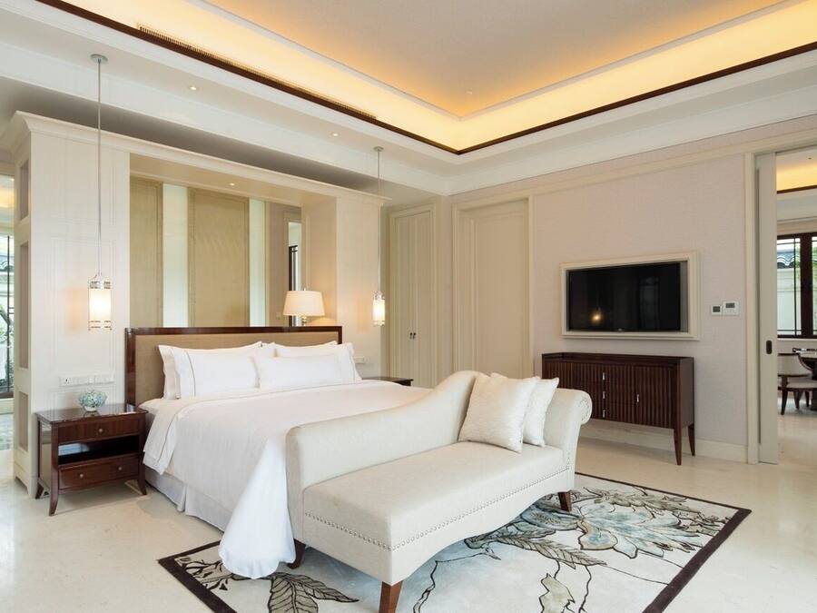 Un dormitorio amplio con una cama grande, un sofá, un televisor y un comedor visible a través de una puerta abierta.