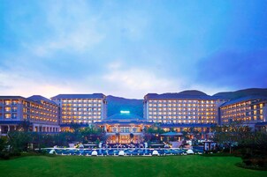 Un hotel grande con varias construcciones, una entrada principal y un césped bien cuidado con zona de piscina.