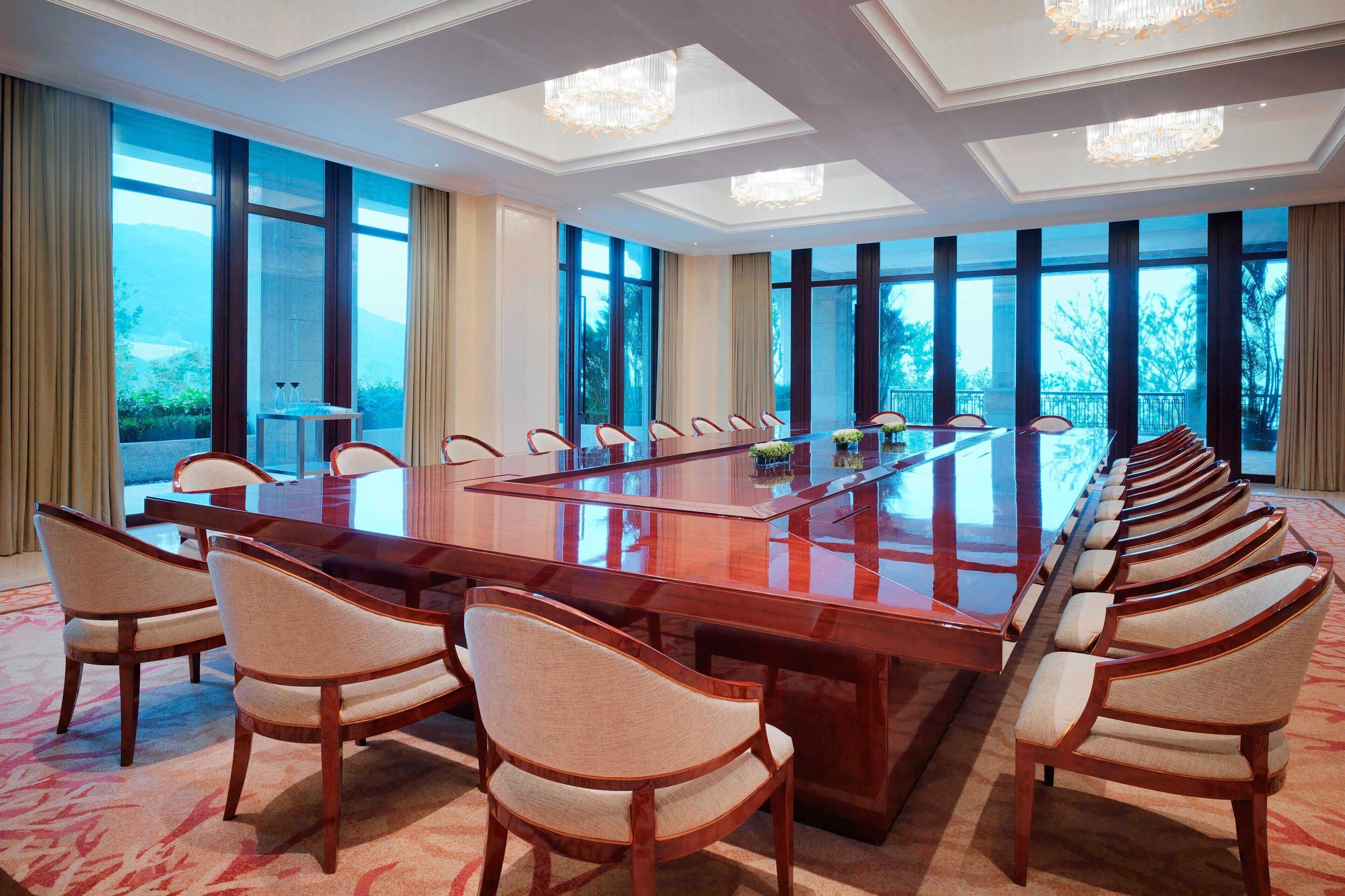 A conference room with a long table and chairs, large windows, and chandeliers.