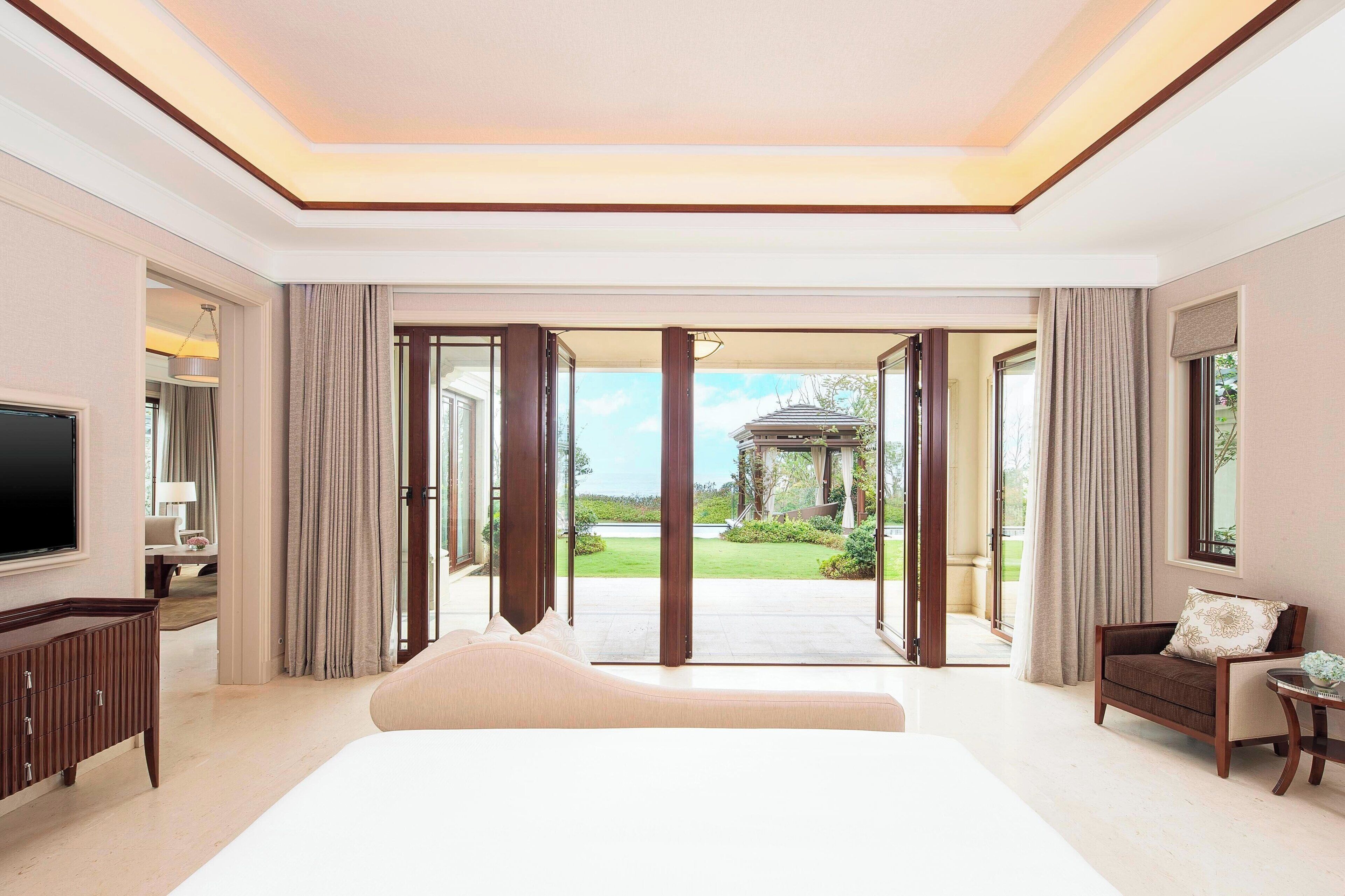 A spacious bedroom with a large bed, a TV, and a view of a garden through a glass door.