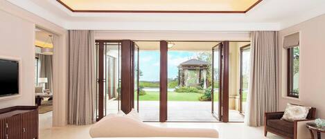 A spacious bedroom with a large bed, a TV, and a view of a garden through a glass door.