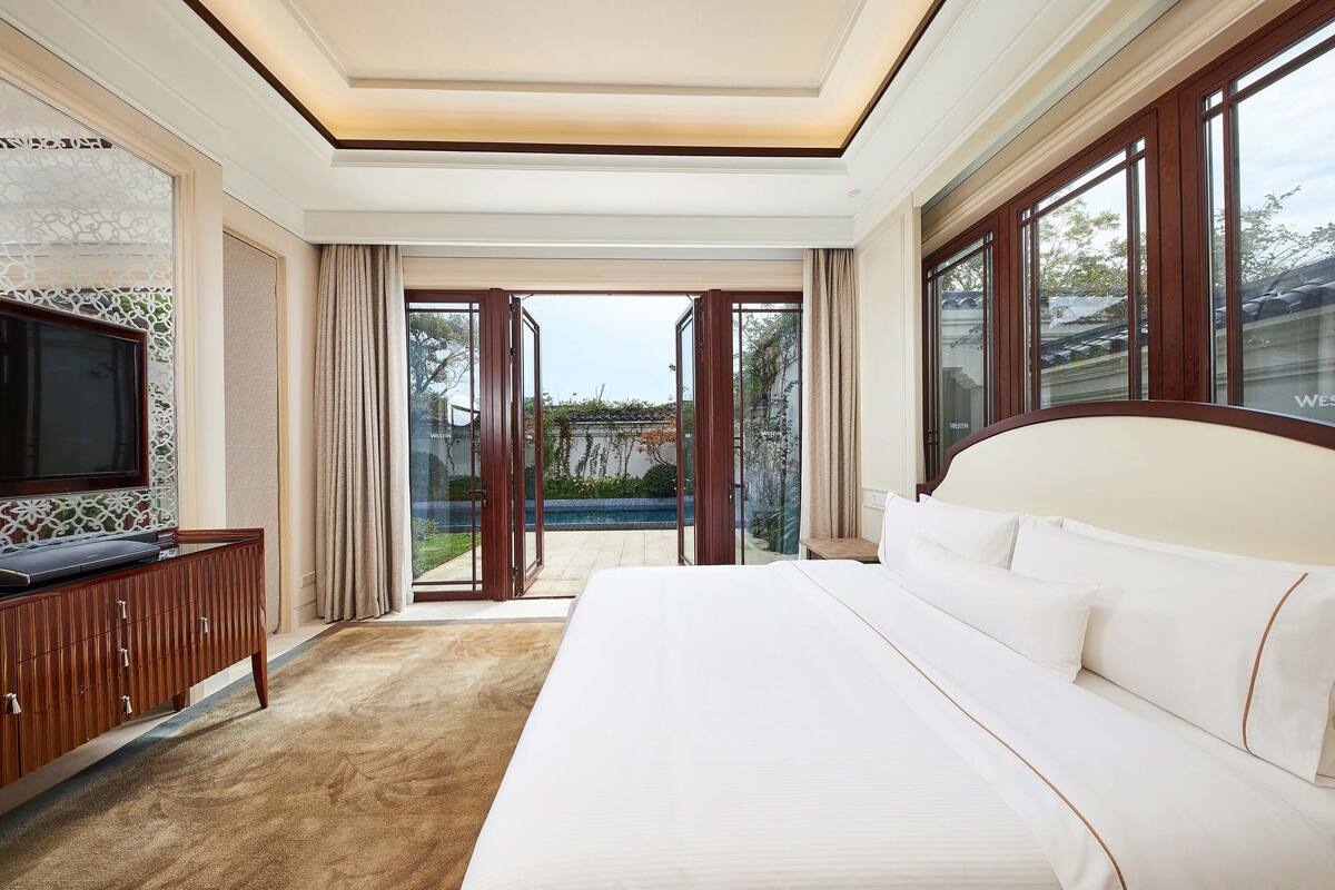 Une chambre d’hôtel avec un grand lit, une télévision et une vue sur une piscine.