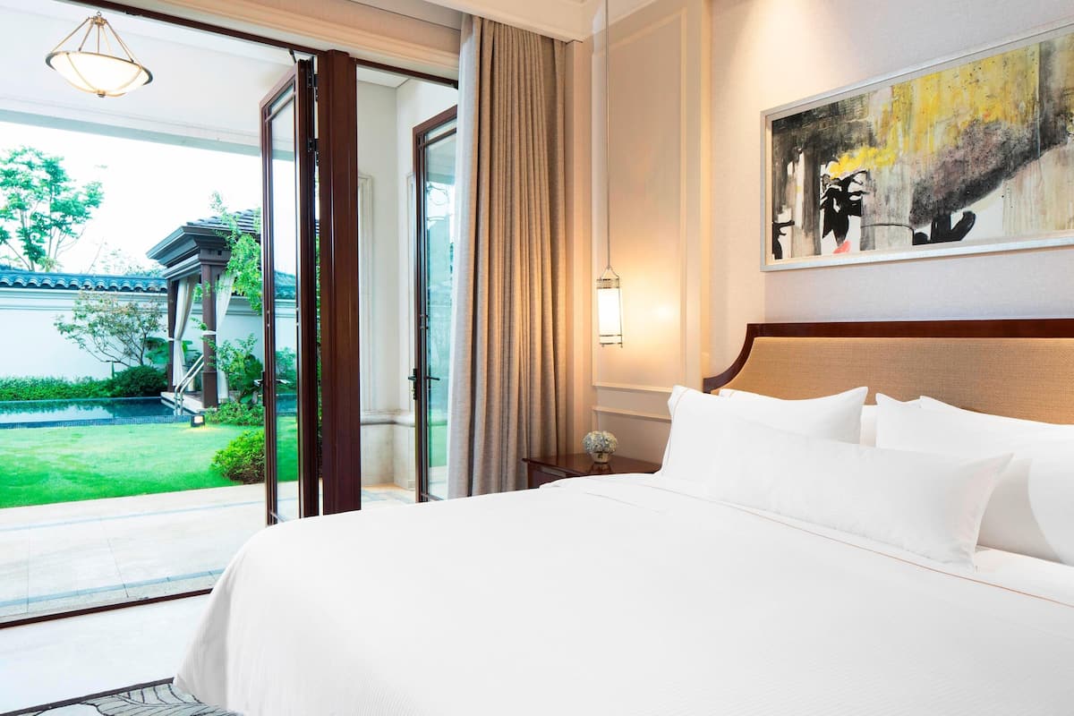 Une chambre d’hôtel avec un grand lit, un tableau au mur et une vue sur un immeuble et la verdure environnante.