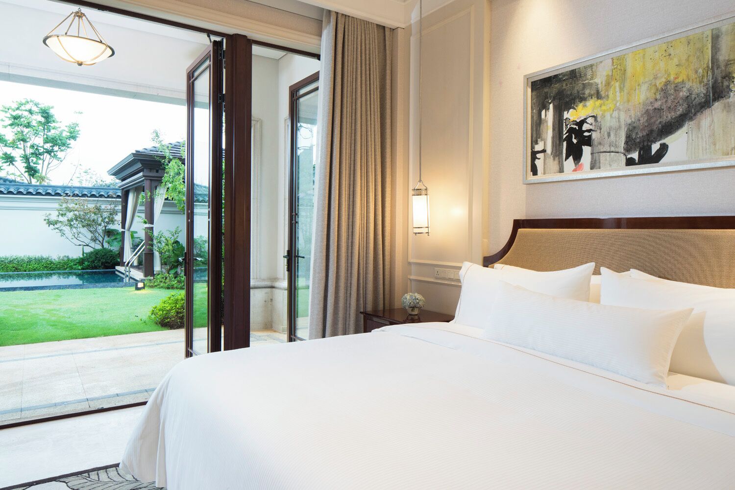 Camera d'albergo con un letto grande, un quadro appeso al muro e vista su giardino e piscina.