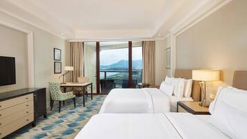 A hotel room with two beds, a desk, a chair, and a TV.