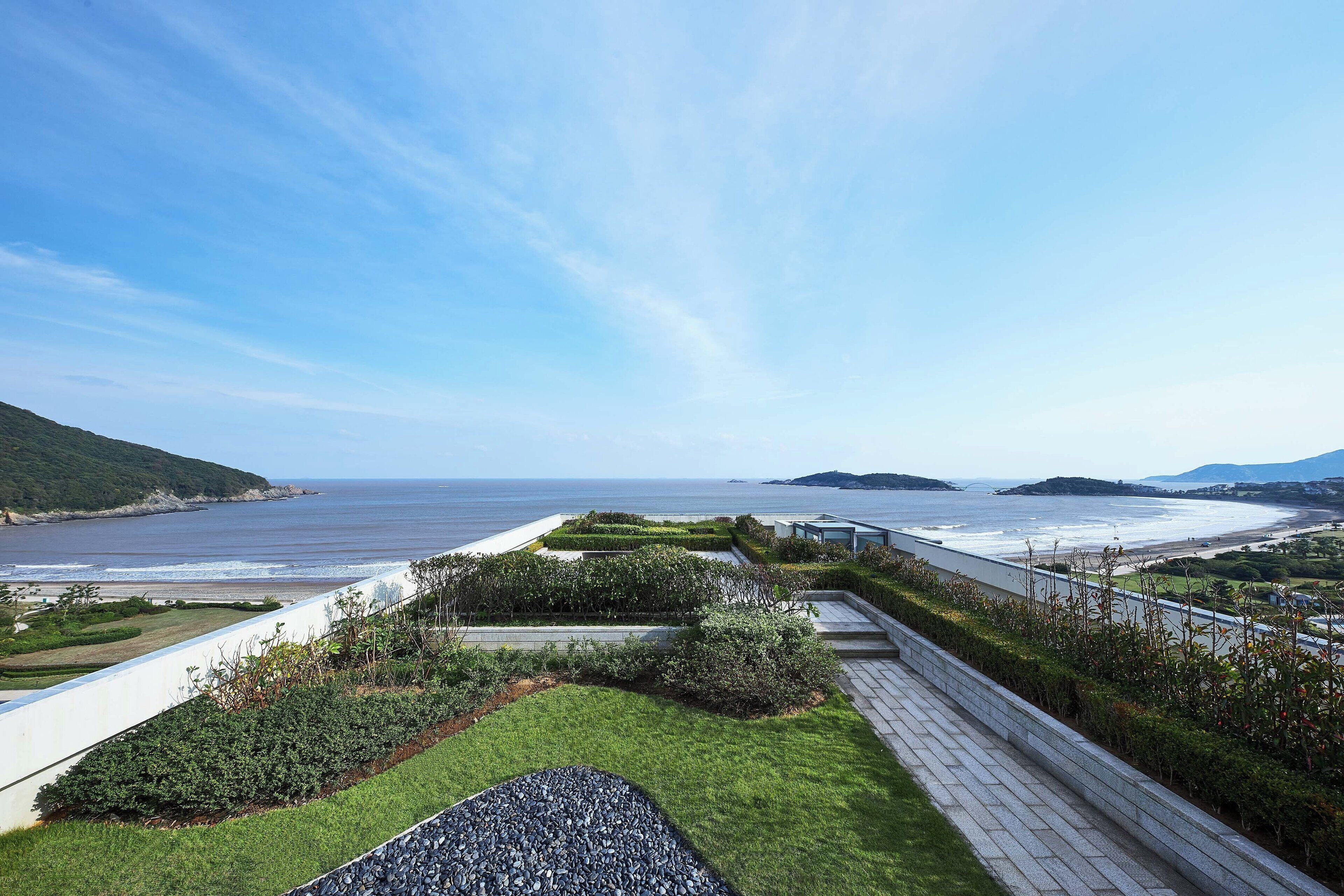 A coastal landscape with a paved walkway, grassy areas, and a view of the sea.