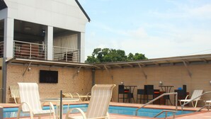 Ein Poolbereich im Freien mit Liegestühlen und Tischen, einer Ziegelwand und einem Gebäude mit Balkon.