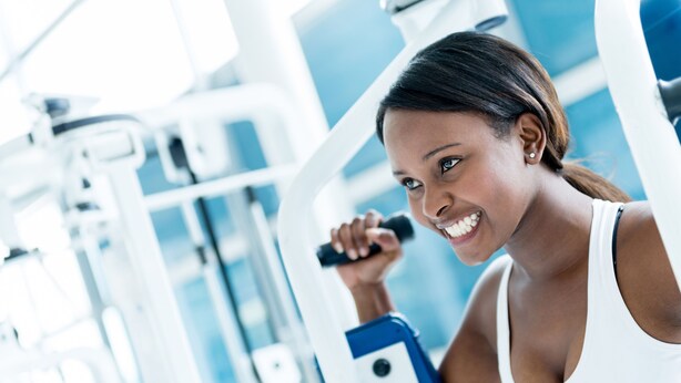 Eine Person trainiert mit Fitnessgeräten in einem hellen Raum mit großen Fenstern.