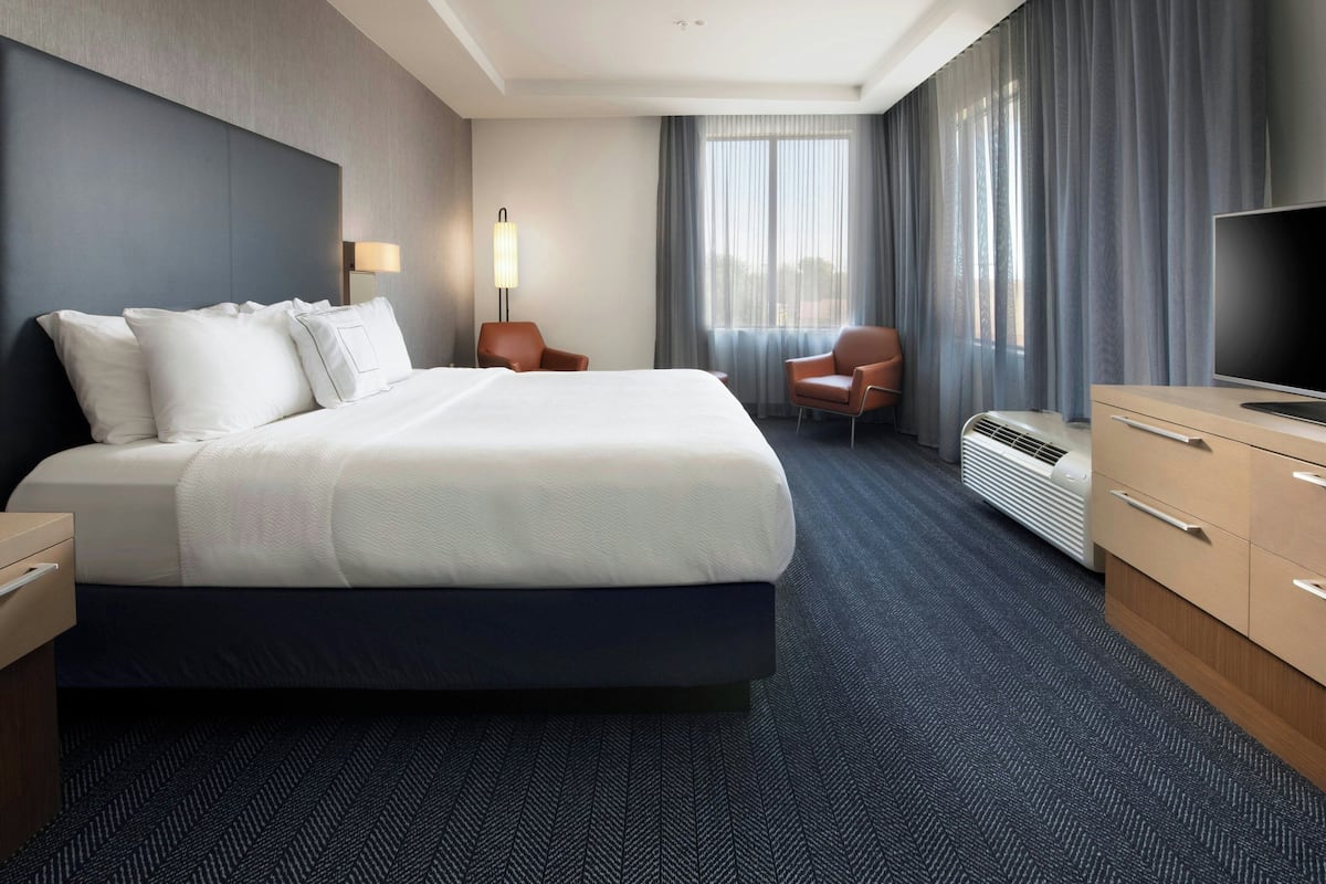 Habitación de hotel con una cama grande, un escritorio, una silla, un televisor y una ventana con cortinas.