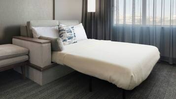 A hotel room with a bed, a nightstand, a chair, a lamp, and a window with curtains.
